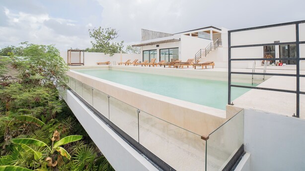 A modern pool area with a glass balustrade, lounge chairs, and a staircase leading to an upper level. - Wellness Suite with Spa, Gym & Rooftop (Tulum)
