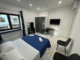 Una camera d'albergo con un letto, una scrivania, una sedia, un armadio, una televisione e una finestra con tende.