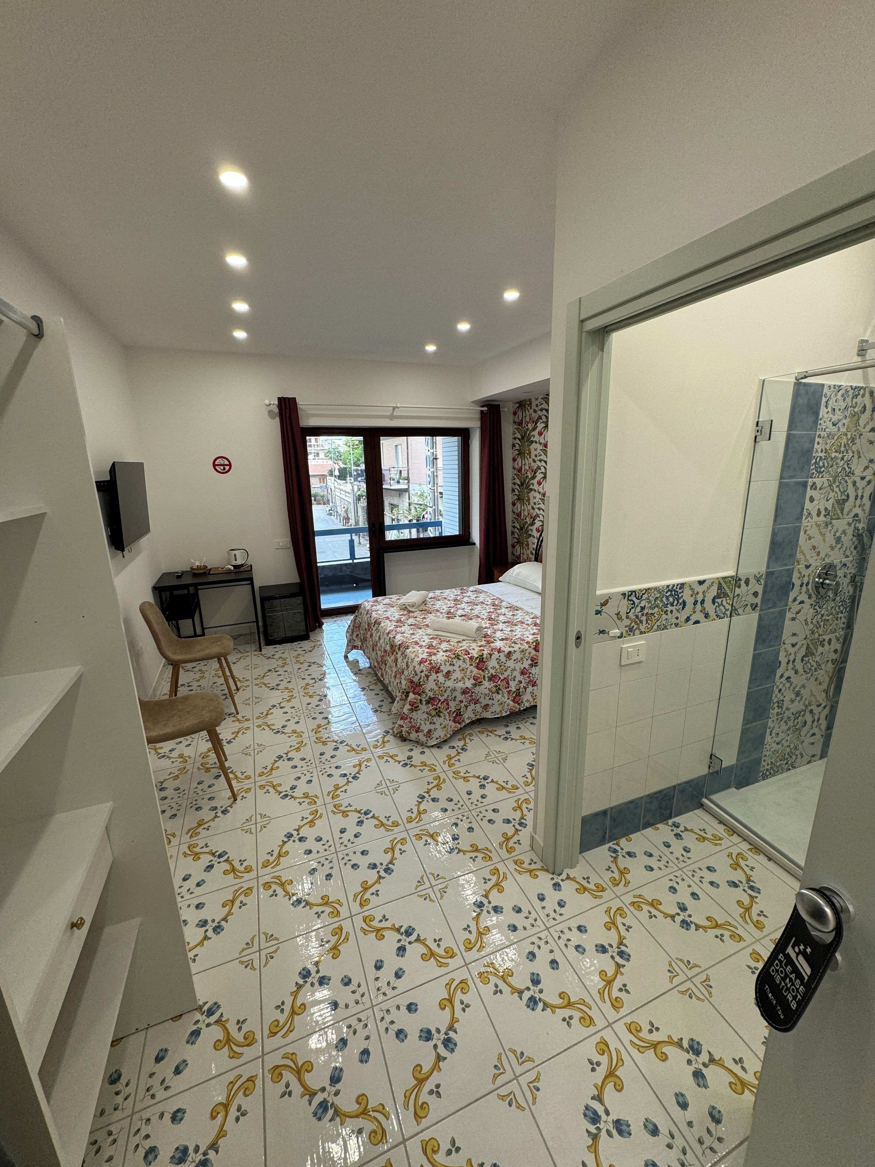 A hotel room with a bed, a desk, a chair, and a bathroom with a shower and toilet.
