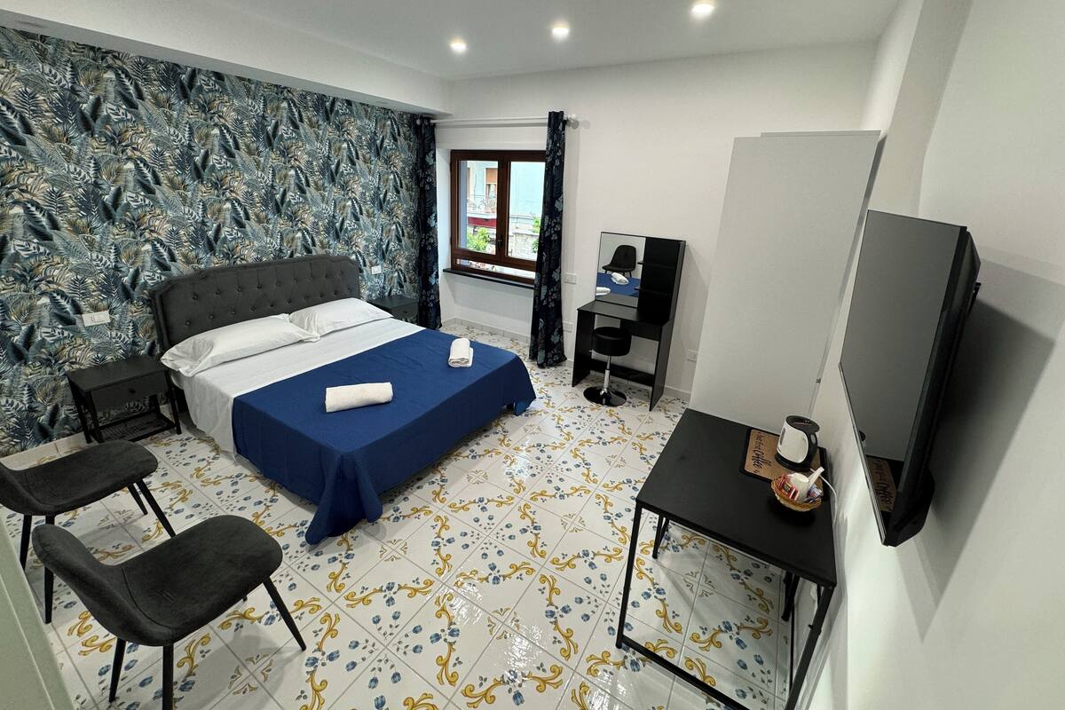 Une chambre à coucher avec un lit, un bureau, une chaise, un téléviseur et une fenêtre avec des rideaux.