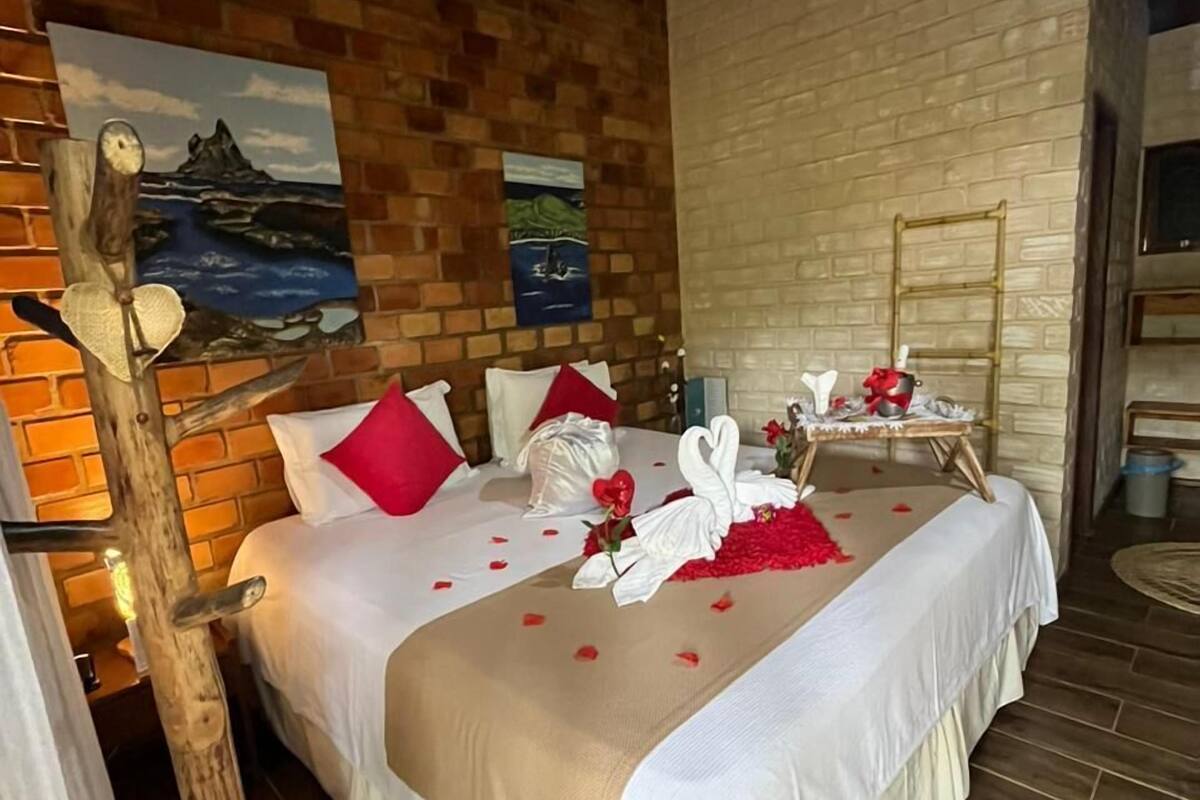 Une chambre bien aménagée avec une tête de lit en bois, un lit avec une literie blanche et rouge, une échelle en bois et un tableau représentant un paysage côtier.