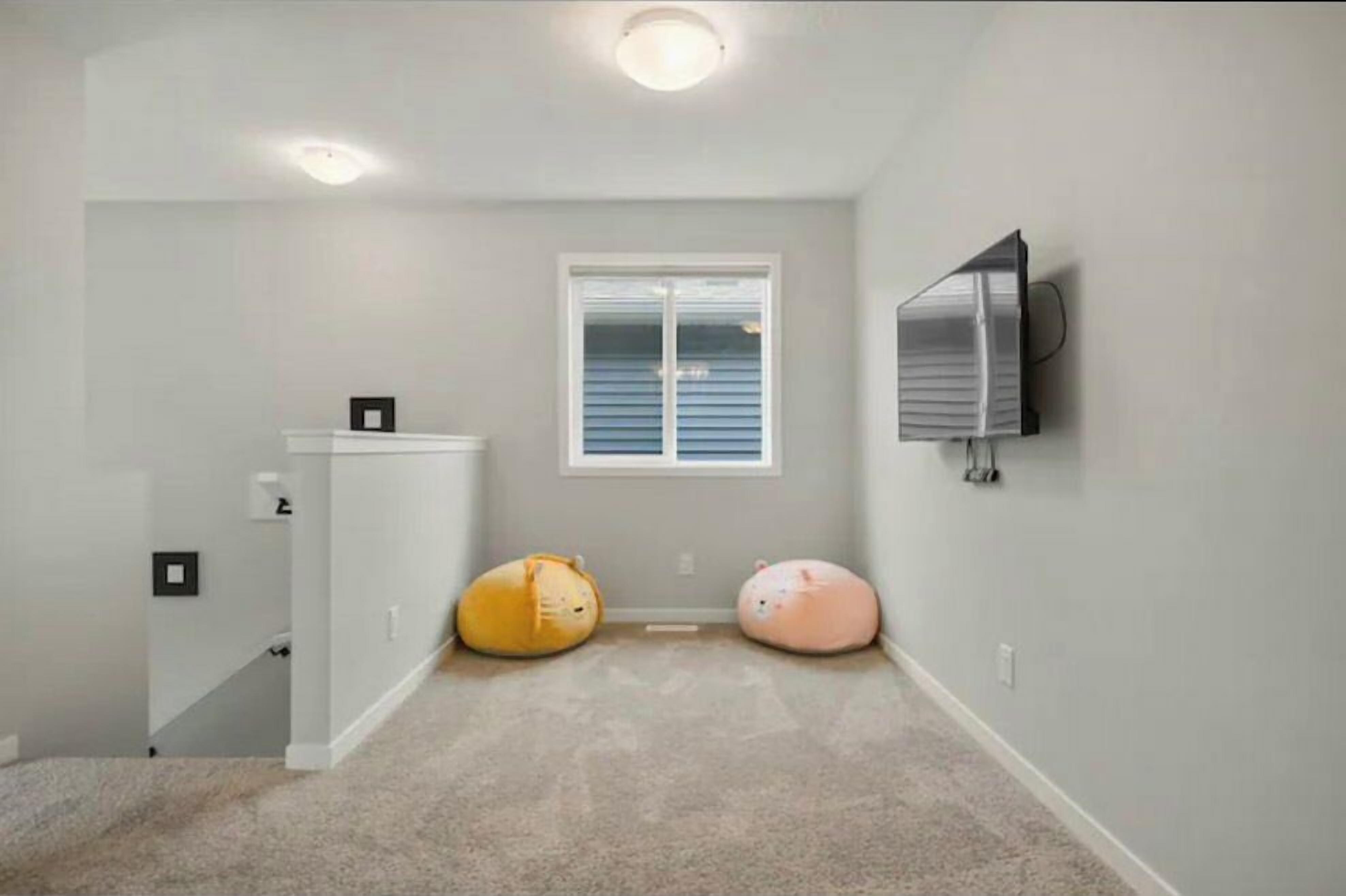 A room with a white wall, a window with blinds, a mounted TV, and two bean bags.