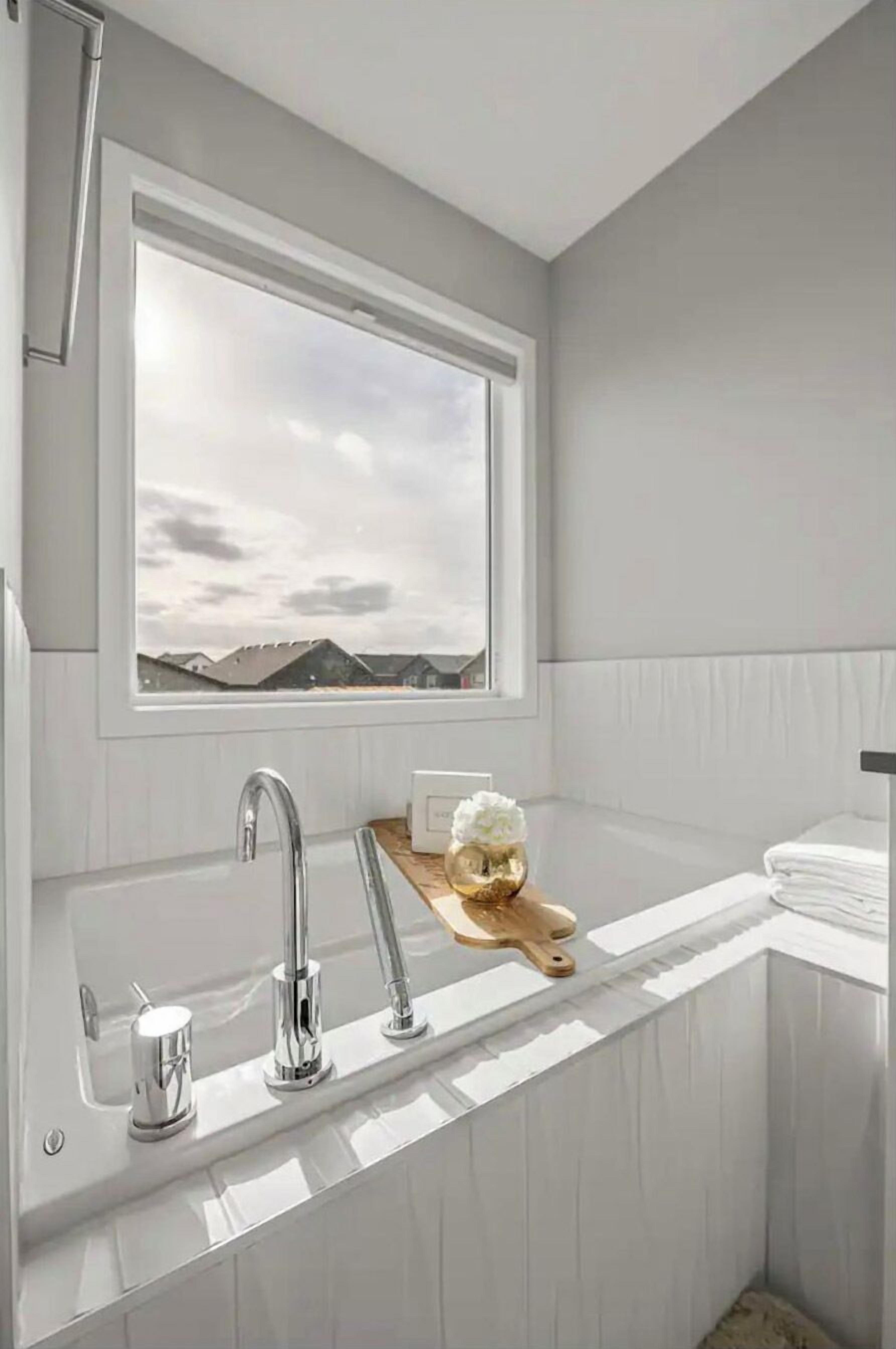 Ein modernes Badezimmer mit großem Fenster, einer freistehenden Badewanne und einem Holzschneidebrett mit Obstschale.