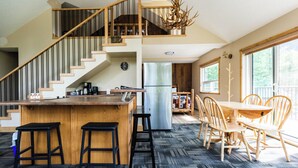 Una cocina amplia con una isla central, taburetes de madera, una escalera y un comedor con sillas y mesa de madera.