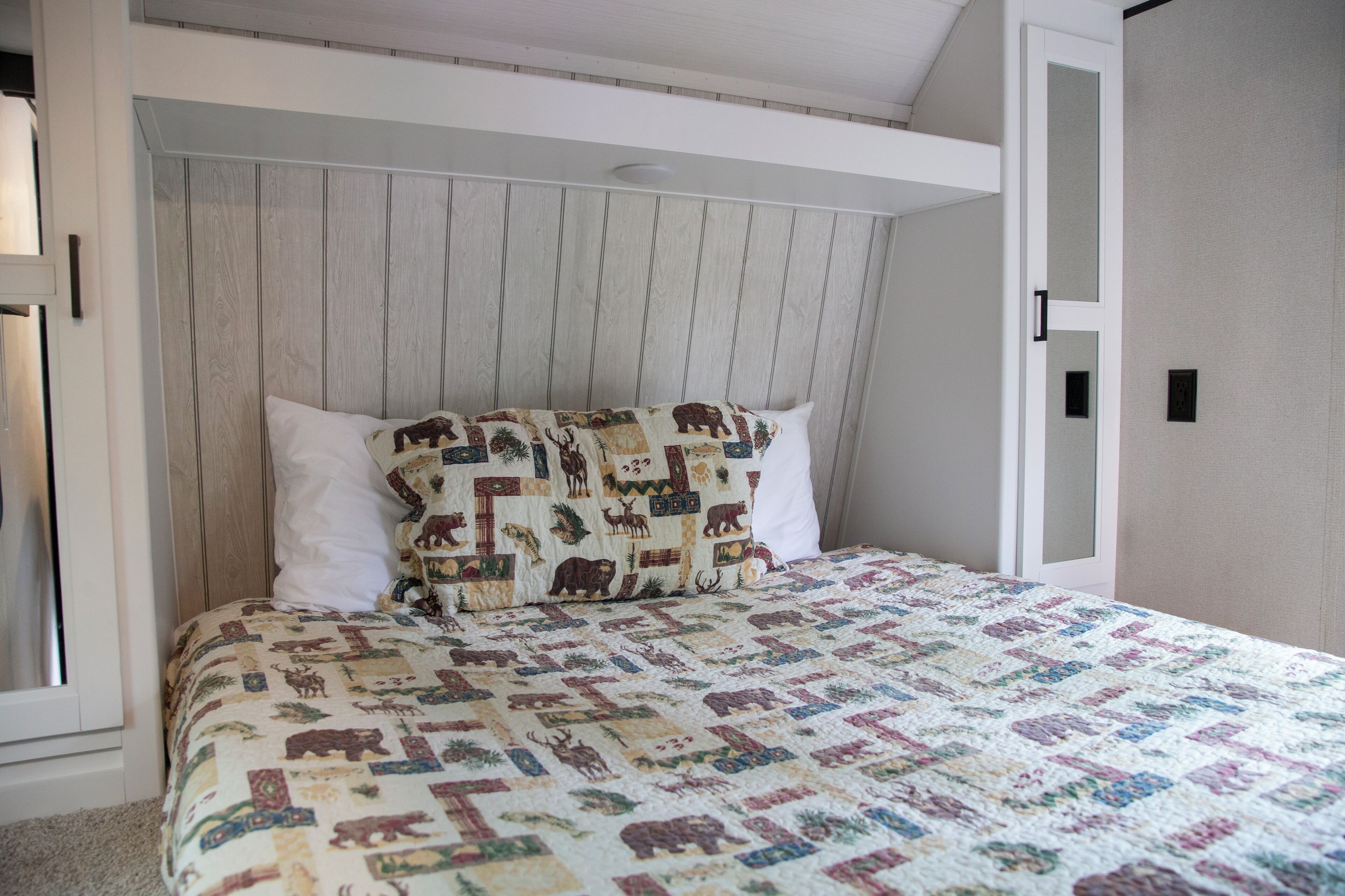 Quarto com cabeceira de madeira, colcha acolchoada com estampas de animais e almofadas brancas.
