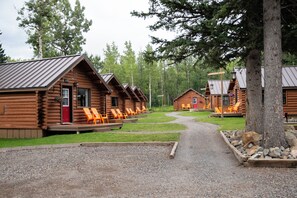 A row of log cabins with outdoor seating areas and a gravel path leading through.