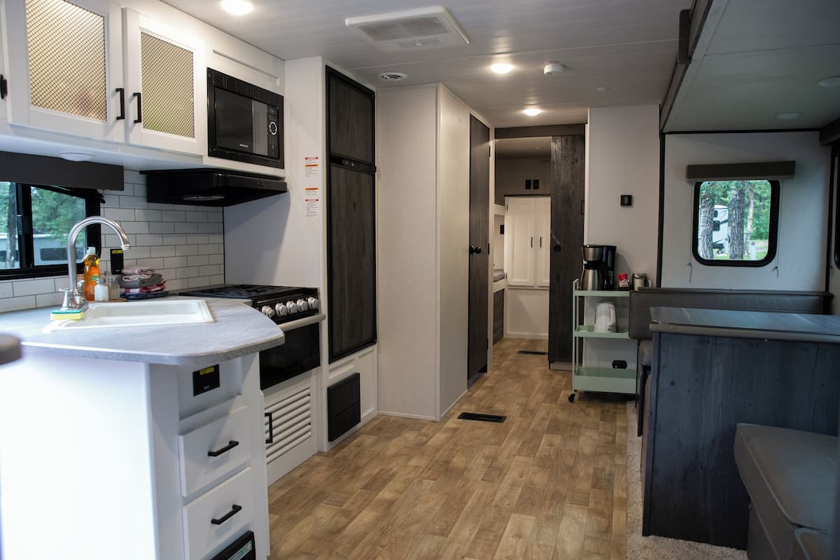 A compact kitchen with white cabinets, a microwave, and a stove. There is a window providing natural light and a view of the outdoors.