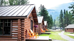 Cabañas de madera con terrazas de madera y sillones naranja, rodeadas de follaje y montañas.
