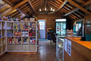 A rustic interior with wooden beams, a central chandelier, and shelves stocked with various items.