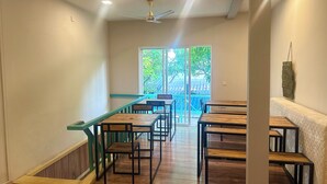 A spacious room with a long table and chairs, a ceiling fan, and a view through a large window. - AAN Beach View (Gulhi)