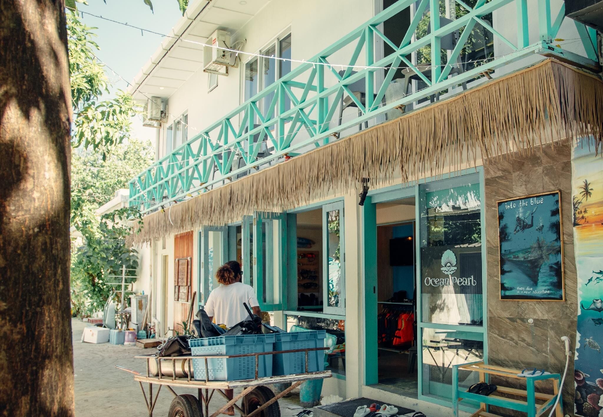 Un bâtiment à la façade bleue, doté d’un toit de chaume et d’une enseigne indiquant « Ocean Pearl Diving ».