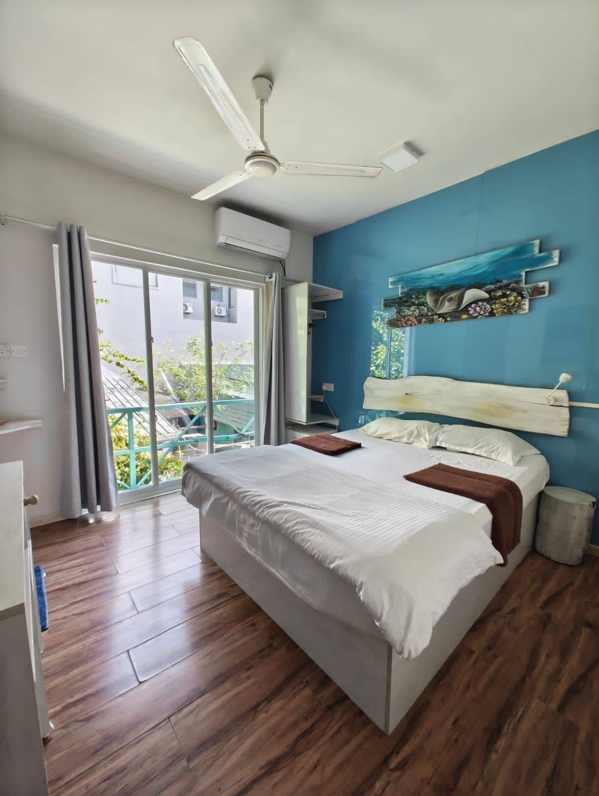 A bedroom with a bed, a ceiling fan, a window with curtains, and a view of greenery outside.