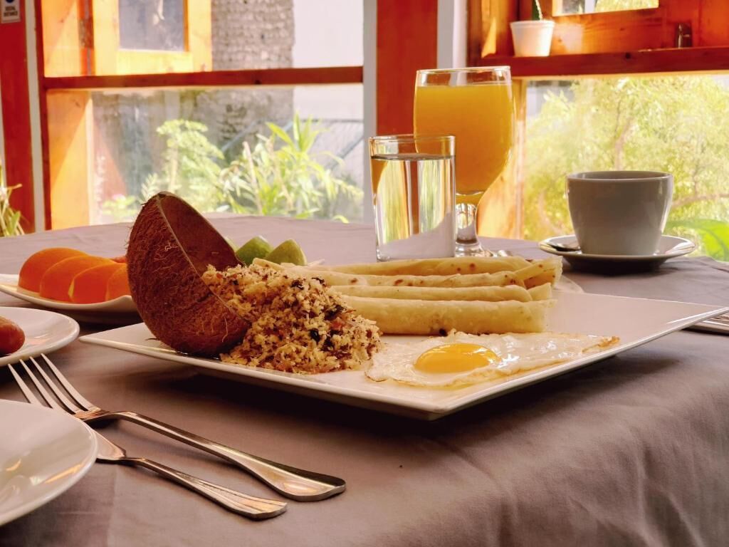 A breakfast plate with fried rice, a fried egg, and a coconut. There are glasses of orange juice and water, and a cup on the table.