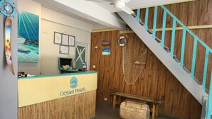 A reception area with a wooden desk labeled "Ocean Pearl," a wooden staircase, and a wall with nautical decorations. - AAN Beach View (Gulhi)