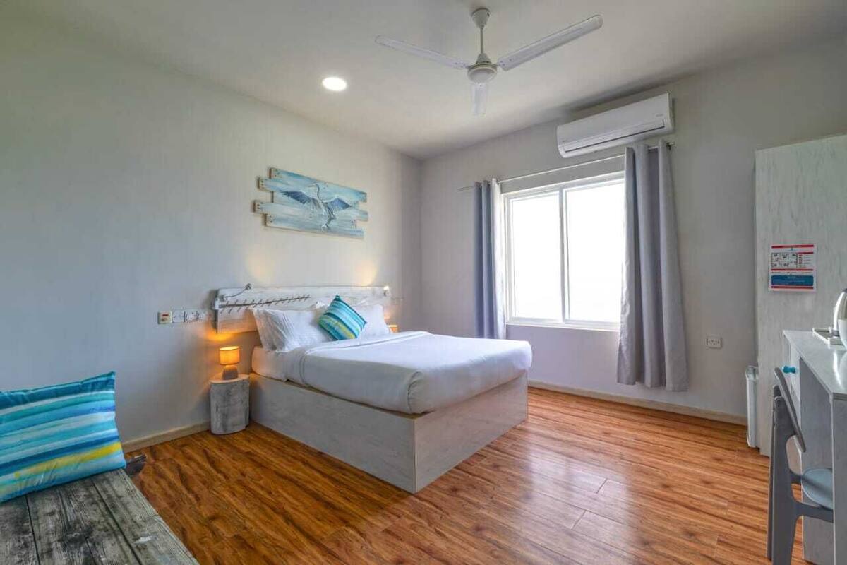 A bedroom with a bed, bedside lamps, a ceiling fan, a window with curtains, and a wooden floor.