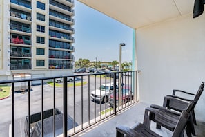 A balcony with a view of a parking lot and a multi-story building with balconies.