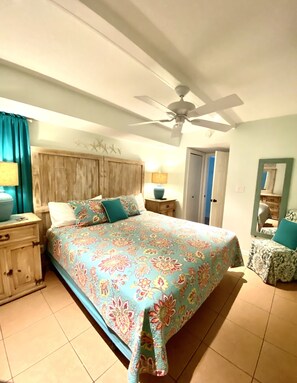 Une chambre à coucher avec un lit, une table de chevet, un ventilateur de plafond et une porte.