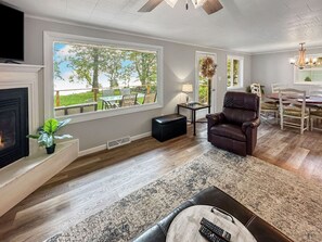 A living room with a fireplace, a leather armchair, a dining area with a table and chairs, and a large window with a view of the outdoors. - Charming 3-bedroom house on the water with AC and WiFi in enjoyable Marinette (Marinette)