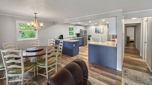 A spacious living area with a dining table, chairs, a sofa, and a kitchen area with blue cabinets and a central island.