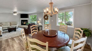 A dining area with a round wooden table, six chairs with floral upholstery, a chandelier, and a fireplace.