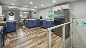 A modern kitchen with blue cabinets, a stainless steel refrigerator, and a herringbone wood floor.