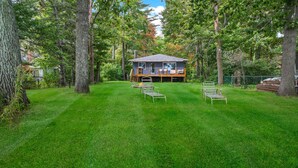 A house with a deck, surrounded by trees and a well-maintained lawn.