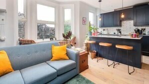Una cocina moderna con barra, un sofá azul con cojines amarillos y ventanas amplias.