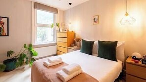 Una cama bien hecha con toallas, una mesita de noche con una lámpara y una ventana con cortinas.