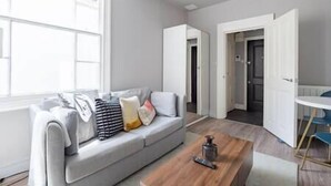 Una sala de estar moderna con un sofá gris, una mesa de centro de madera y vistas a un pasillo.