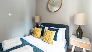 Habitación de hotel con una cama, dos lámparas de noche, una mesita de noche y un espejo redondo en la pared.