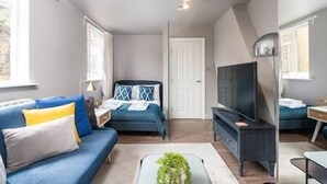 Una habitación moderna y luminosa, con sofá, cama, televisor y una mesita.