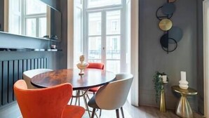 A dining area with a round table, two chairs, a vase, and a wall-mounted light fixture.