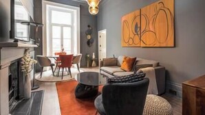 A modern living room with a fireplace, a dining area, and a large abstract painting on the wall.