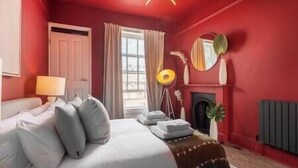 Ein Schlafzimmer mit roten Wänden, einem Bett, einer Lampe, einem Spiegel und einem Kamin.