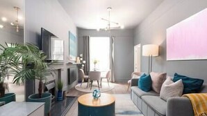 Ein modernes Wohnzimmer mit grauem Sofa, einem Couchtisch und einem Fernseher. Eine Pflanze, eine Lampe und ein Gemälde zieren die Wand.