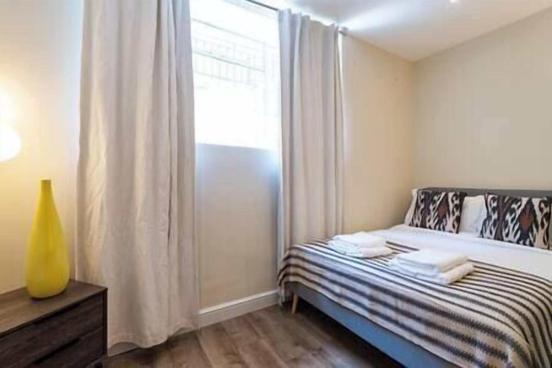 A bedroom with a bed, curtains, a bedside table, and a lamp.