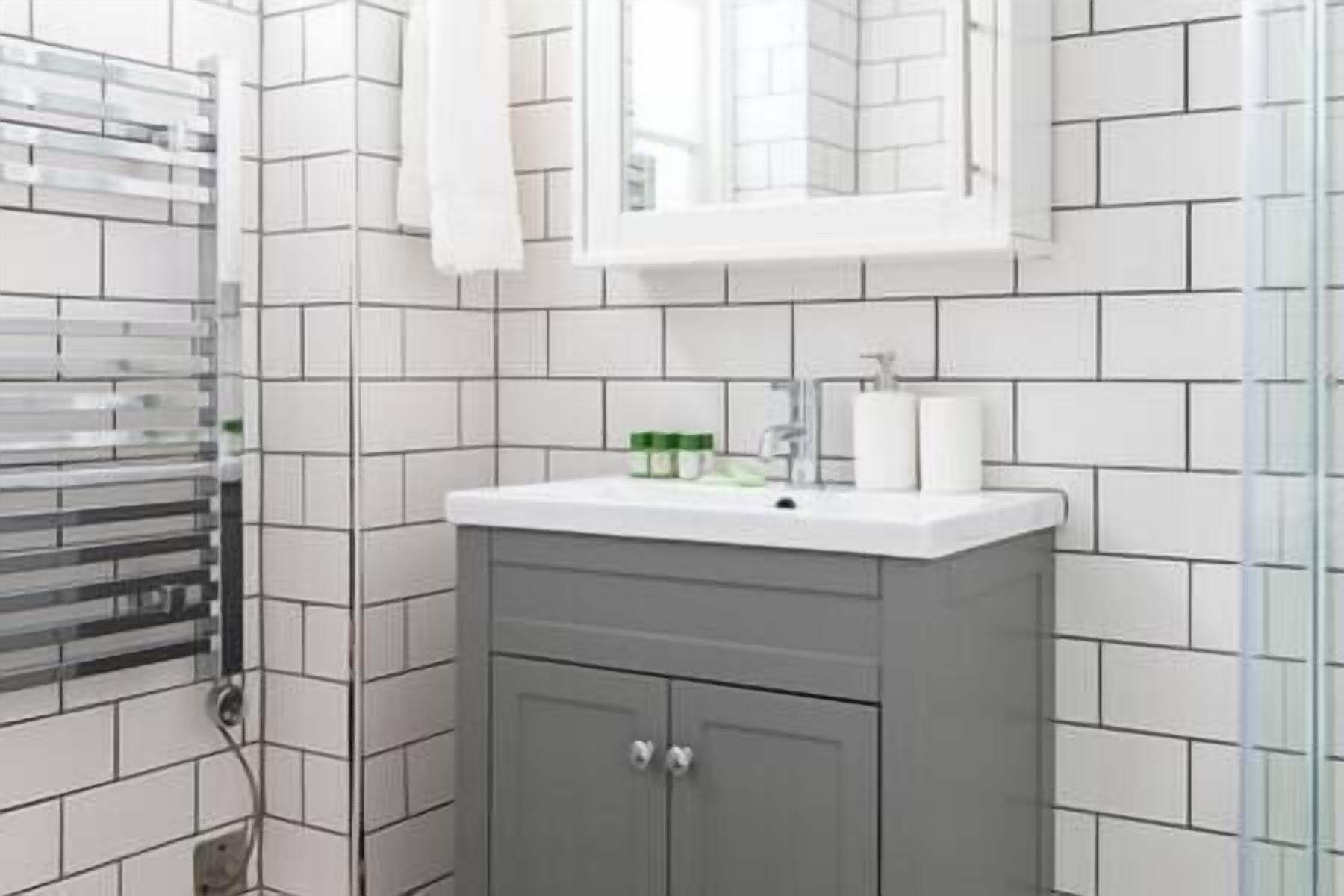 A bathroom with white tiled walls, a white sink, and a mirror above it.