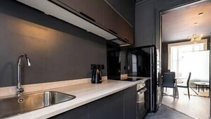 Eine moderne Küche mit einem schlanken, schwarzen Kühlschrank, einer Edelstahl-Spüle und einer hellen Arbeitsplatte.