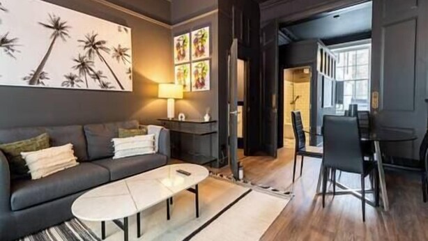 Ein modernes Wohnzimmer mit einem dunkelgrauen Sofa, einem runden Couchtisch und einem Essbereich mit Tisch und Stühlen.