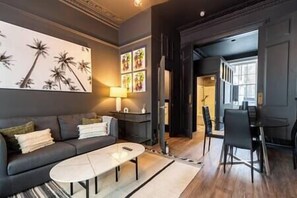 Un salon moderne avec un canapé de couleur foncée, une table basse ronde et un coin repas comprenant une table et des chaises.
