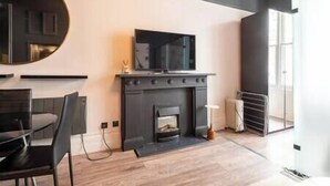 Ein modernes Wohnzimmer mit Kamin, einem flachbildfernseher darüber und einem Essbereich mit Tisch und Stühlen.