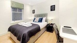 Ein modernes Hotelzimmer mit Bett, Nachttisch, Schreibtisch und einem Fenster mit Jalousien.