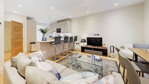 Un salon moderne avec un canapé, une table basse en verre et un téléviseur. Il y a également un coin cuisine avec une table à manger et des chaises.