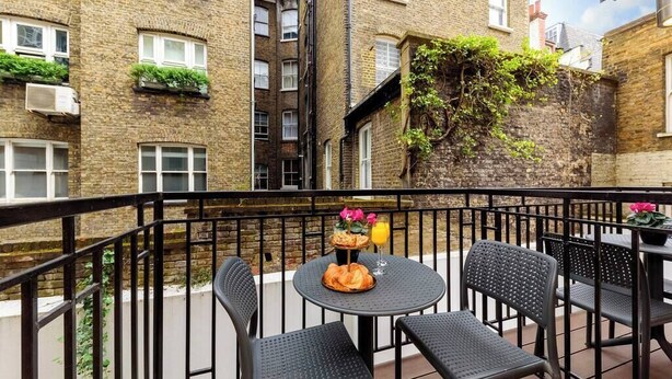 A courtyard with a round table and four chairs, surrounded by a black metal railing. - PBC | Modern Two Bedroom Apartment in Soho - GT3 (London)