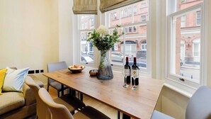 A dining area with a wooden table, chairs, a vase with flowers, and two bottles of wine. - PBC | Modern Two Bedroom Apartment in Soho - GT3 (London)