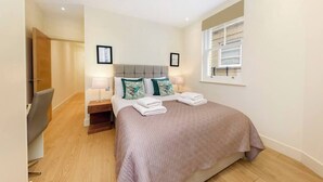 A neatly arranged bedroom with a bed, bedside lamps, and a window. - PBC | Modern Two Bedroom Apartment in Soho - GT3 (London)
