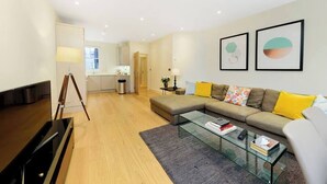 A modern living room with a sectional sofa, a glass coffee table, and a flat-screen TV. - PBC | Modern Two Bedroom Apartment in Soho - GT3 (London)
