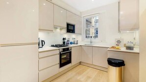 A modern kitchen with white cabinets, a microwave, a stove, and a trash can. - PBC | Modern Two Bedroom Apartment in Soho - GT3 (London)