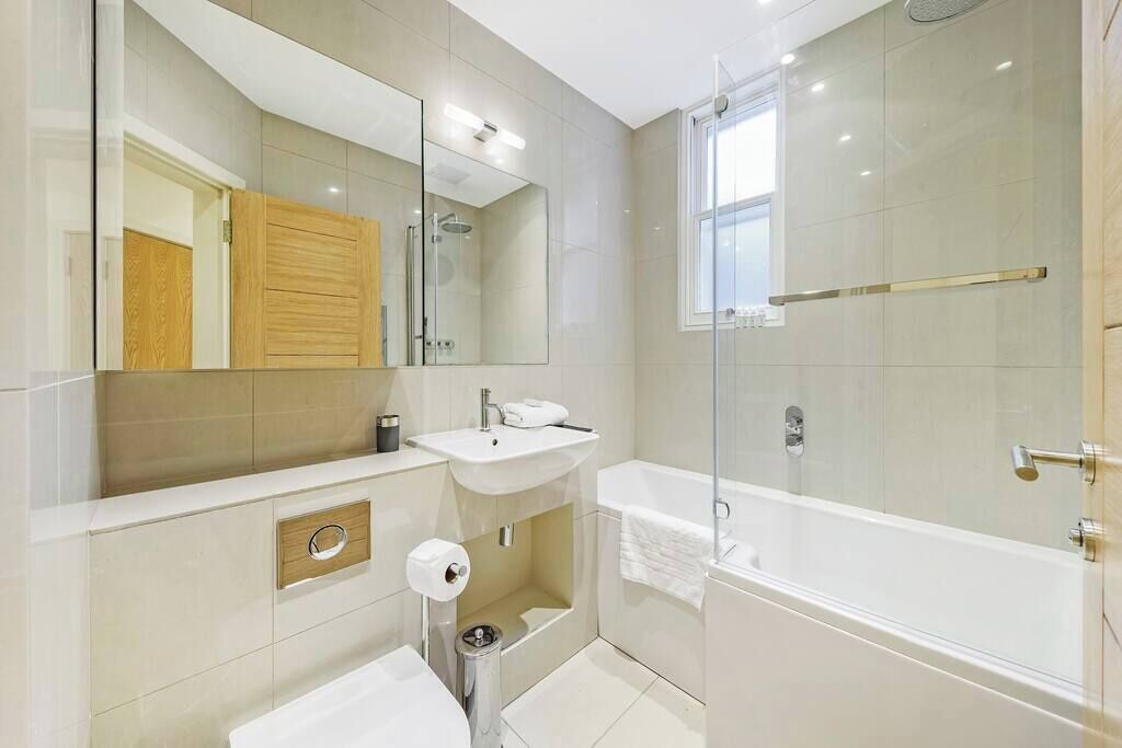 A modern bathroom with a large mirror, a sink, a toilet, and a walk-in shower.