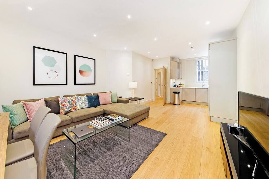 A modern living room with a sectional sofa, a glass coffee table, and a kitchen in the background.